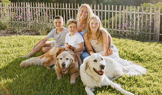 Mel, founder of Cooper and Kids, sitting on the grass with her three children and two golden retrievers.