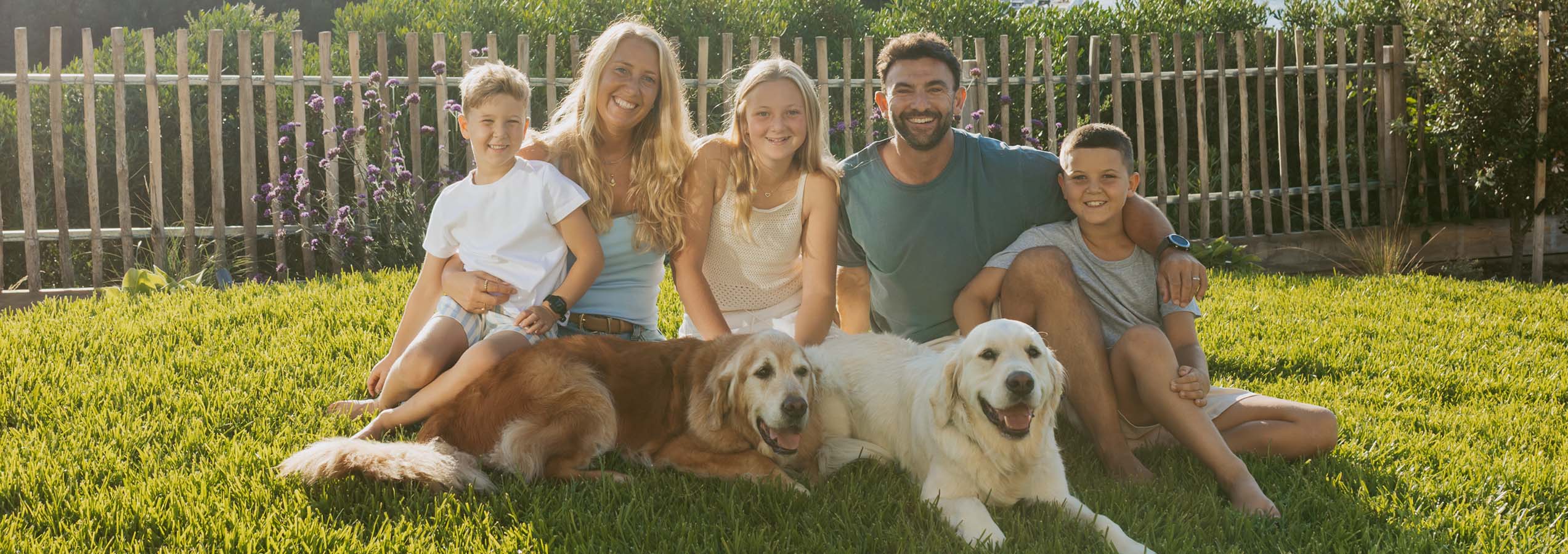Mel, founder of Cooper and Kids, sitting on the grass with her three children and two golden retrievers.